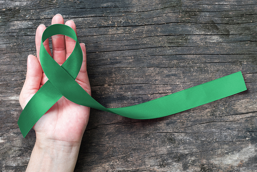 Top view of emerald green ribbon on dark wood background. Liver cancer  awareness concept. - Futurity